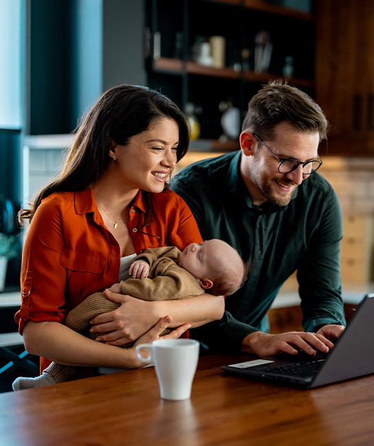 Young couple with a baby looking at a laptop smiling at kitchen island