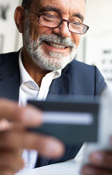 Man in suit in his 60s smiling while holding a credit card