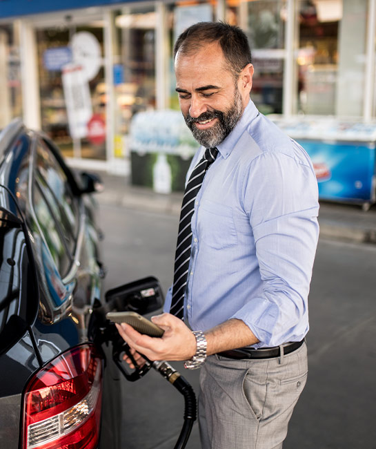 Man pumping gas while holding phone