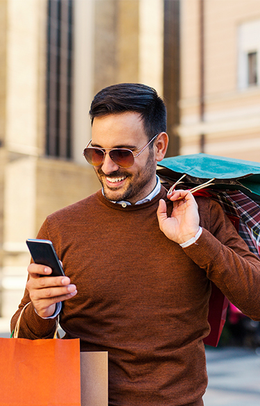 Man smiling looking at his phone holding shopping bags