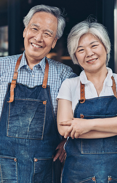 Older couple standing in front of their business smiling at the camera