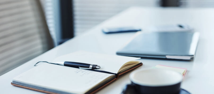 A desk with notebook, coffee, pen, and closed laptop