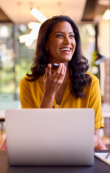 Young business woman using her laptop and phone on speaker smiling