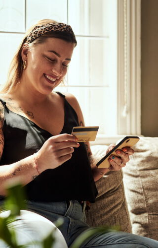 Young woman on couch using phone and debit/credit card