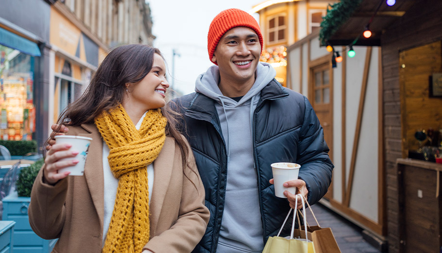 Couple holiday shopping outdoors holding coffee and bags smiling