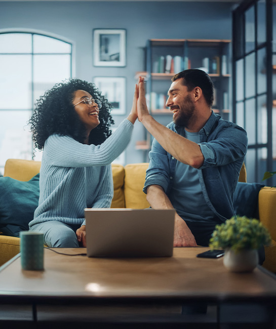 Couple high fiving on their couch with laptop on table in front of them