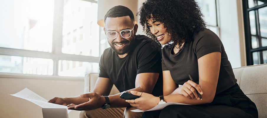 Couple sitting on couch doing finances looking at a laptop smiling 