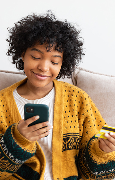 Teenage girl smiling holding a credit card looking at her cell phone