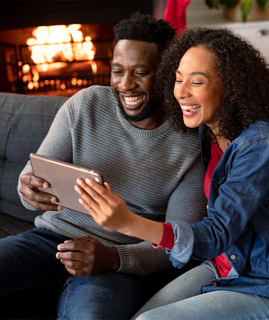 Couple looking at tablet smiling with fireplace in the background