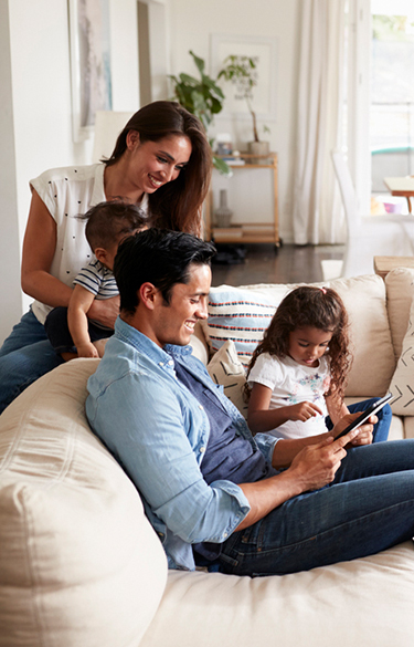 Family sitting on couch while mother and father look at a tablet smiling