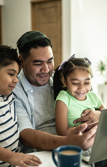 Dad with his two kids sitting at the kitchen table using phone and computer